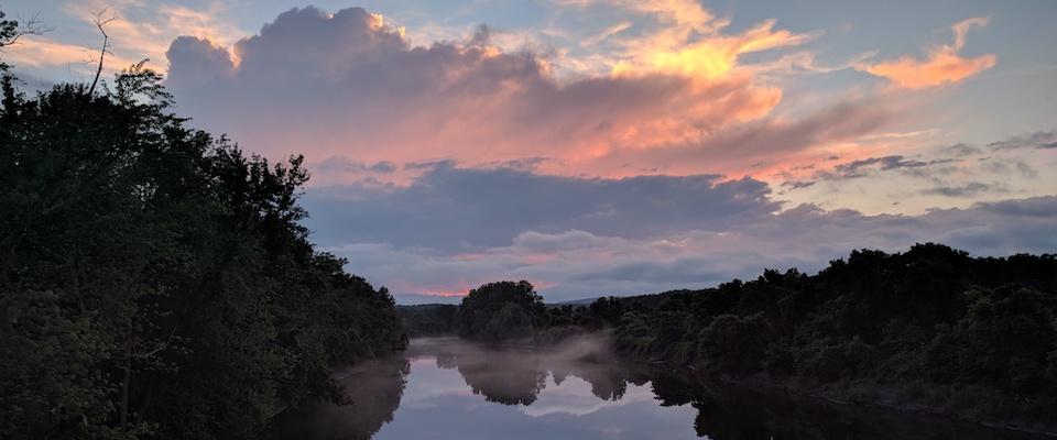 Red-tinted clouds above trees and a river